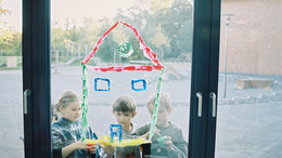 Kinder malen auf dem Fenster einer Schule ein Bild mit Farbe