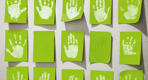 An der Wand einer Kita hängen hellgrüne Blätter Papier, auf denen Kinder in weißer Farbe ihre Handabdrücke hinterlassen haben.