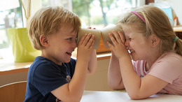 Zwei Kinder sehen sich durch eine Papprolle an.