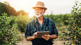[Translate to English:] Ein Landwirt steht in einem Feld und hält ein Tablet in der Hand