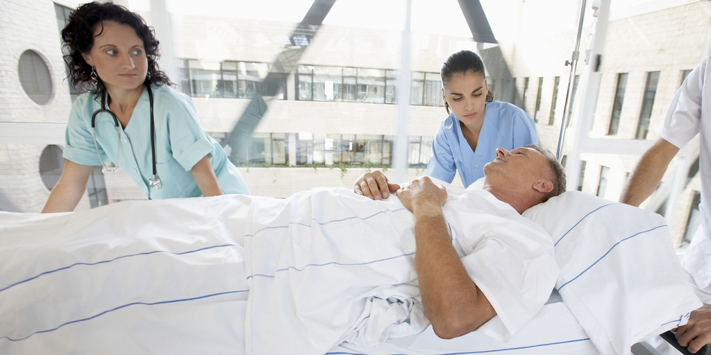 Ein Mann wird in einem Krankenbett von zwei Mitarbeiterinnen eines Krankenhauses geschoben.