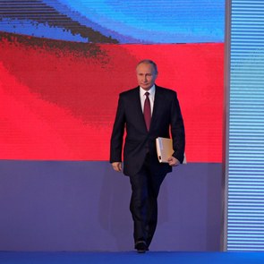 Mit einer Dokumentenmappe unter dem Arm betritt Russlands Präsident Wladimir Putin eine Bühne, hinter der auf einem riesigen Bildschirm eine russische Flagge projiziert wird.