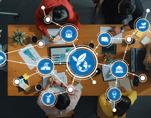 Eine Gruppe von Menschen sitzt an einem Holztisch in einer Besprechung, darüber liegt eine digitale Grafik vernetzter Icons zu den Themen Nachhaltigkeit, Umweltschutz und globale Vernetzung.