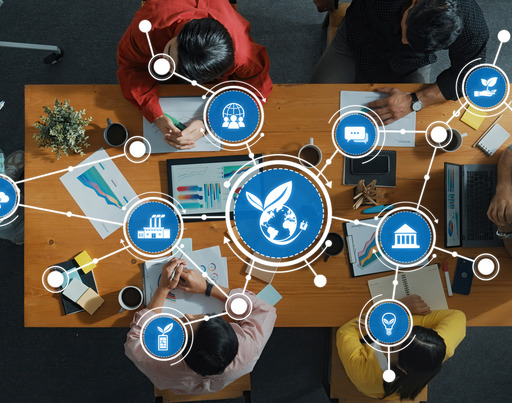 Eine Gruppe von Menschen sitzt an einem Holztisch in einer Besprechung, darüber liegt eine digitale Grafik vernetzter Icons zu den Themen Nachhaltigkeit, Umweltschutz und globale Vernetzung.