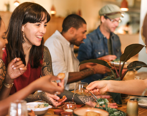 Lächelnde junge Freunde, die gemeinsam in einem angesagten Bistro zu Abend essen. Eine lächelnde Gruppe junger Freunde unterschiedlicher Herkunft, die an einem Tisch in einem angesagten Bistro sitzt und gemeinsam das Essen genießt.