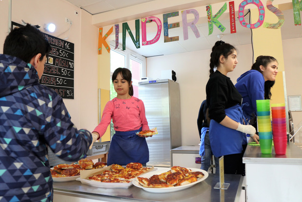 In einem Kinderkiosk verkaufen Schülerinnen anderen Schülern Pizza.