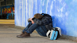 Ein Jugendlicher sitzt auf der Erde, legt seinen Kopf auf die Knie und versteckt sein Gesicht dadurch.