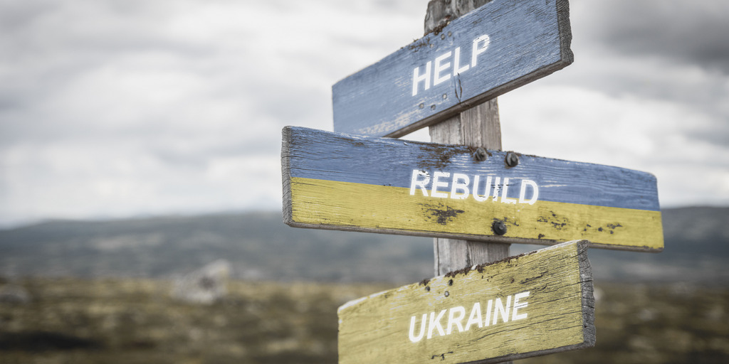 Ein Wegweiser mit drei Schildern: help, rebuild, Ukraine