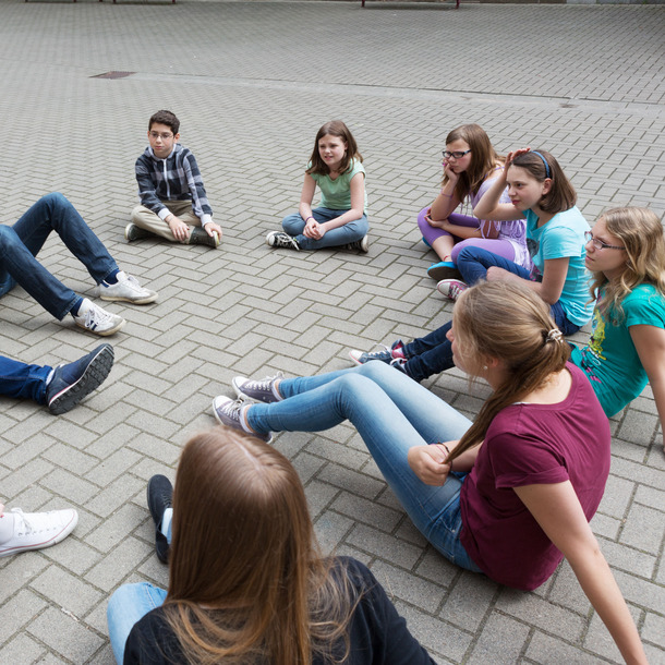 Kinder und Jugendliche sitzen im Kreis auf dem Boden und unterhalten sich