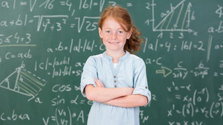 Kleines Mädchen steht vor einer Tafel mit komplizierten Formeln