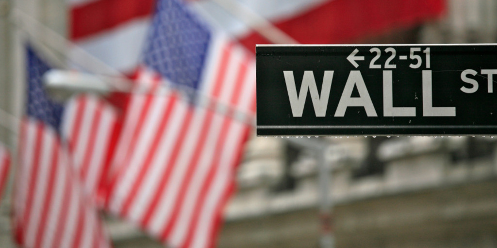 A picture from Wall Street in New York City: In the foreground there is a sign with the name of the street, in the background there are the US flags outside the building of New York Stock Exchange.