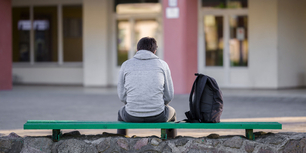 Ein junger Mann sitzt auf einer Bank auf dem Schulhof.