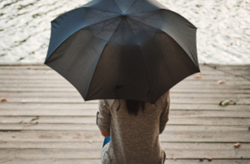 Frau sitzt am Steg auf einer Holzbank mit einem Regenschirm.