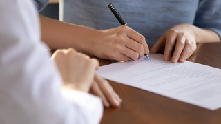 Eine junge Frau unterschreibt einen Arbeitsvertrag