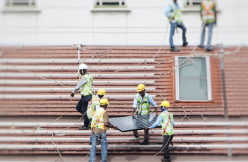 Arbeiter setzen auf einem Dach ein Panel für eine Solaranlage ein.
