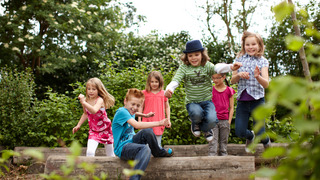 Gruppe fröhlicher Schulkinder, die draußen auf alten Baumstümpfen herumlaufen.