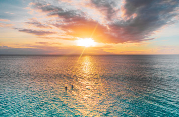 Sonnenuntergang über den Meer - zwei Menschen stehen im Wasser in Richtung Sonne.