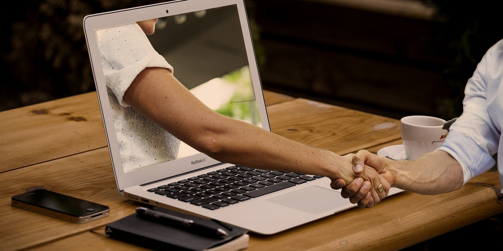 Händedruck mit Hand aus dem Laptop kommend und Hand vor dem Laptop