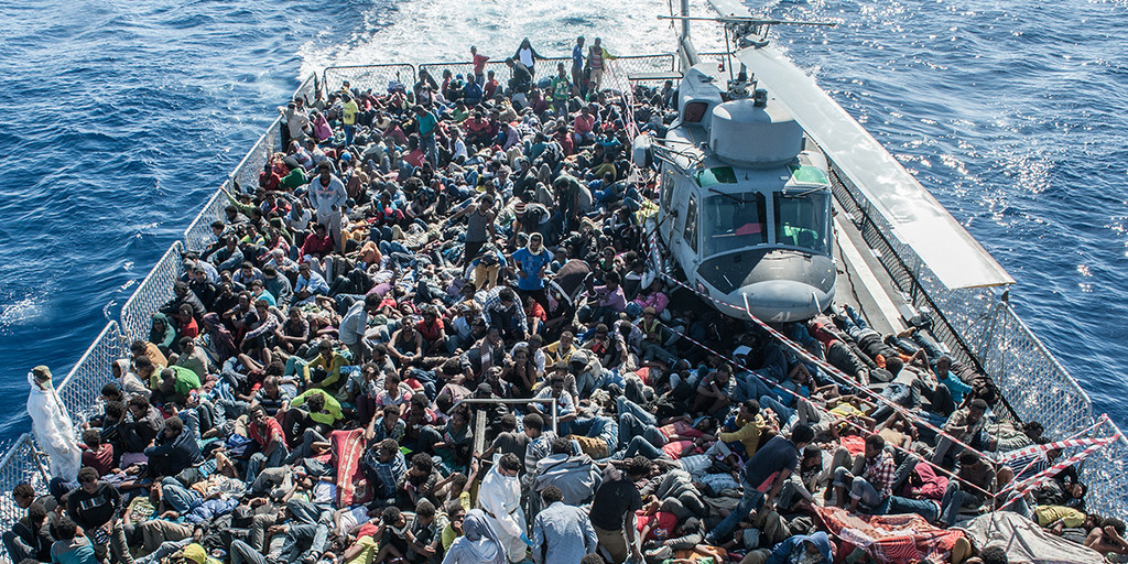 [Translate to English:] Vogelperspektive auf ein Rettungsboot voll mit Flüchtlingen und einem Hubschrauber im Mittelmeer.