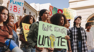 Eine Gruppe junger Menschen steht zusammen auf einer Demonstration. Sie halten ein Schild mit der Aufschrift: We must unite.