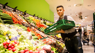 Ein Praktikant im Einzelhandel räumt ein Gemüseregal ein