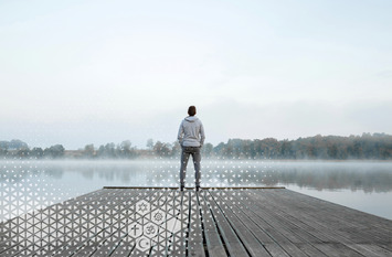Mann steht auf einem Holz-Steg und schaut über den Nebelverhangenen See.