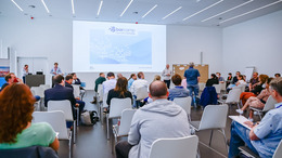 [Translate to English:] Blick von hinten im Raum auf die Teilnehmerinnen des Open-Data-BArcamps 2021 in Bochum. Vorne sind die Moderatoren und Gastgeber und eine Begrüßungsfolie ist an die Wand geworfen.