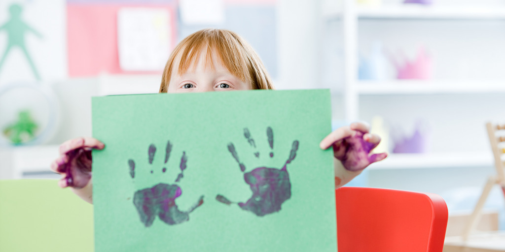 Kind hält ein Bild mit Handabdrücken hoch