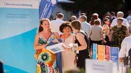 Daniela Schmidt, Projektmanagerin der Bertelsmann Stiftung, unterhält sich am Stand der Stiftung und des Liz Mohn Centers auf dem Bürgerfest des Bundespräsidenten mit zwei Besucherinnen.