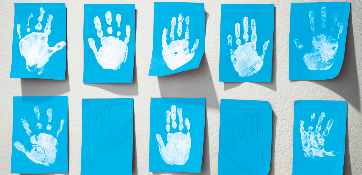 Weiße Abdrücke von Kinderhänden auf blauen Zetteln hängen an der Wand einer Kindertagesstätte.